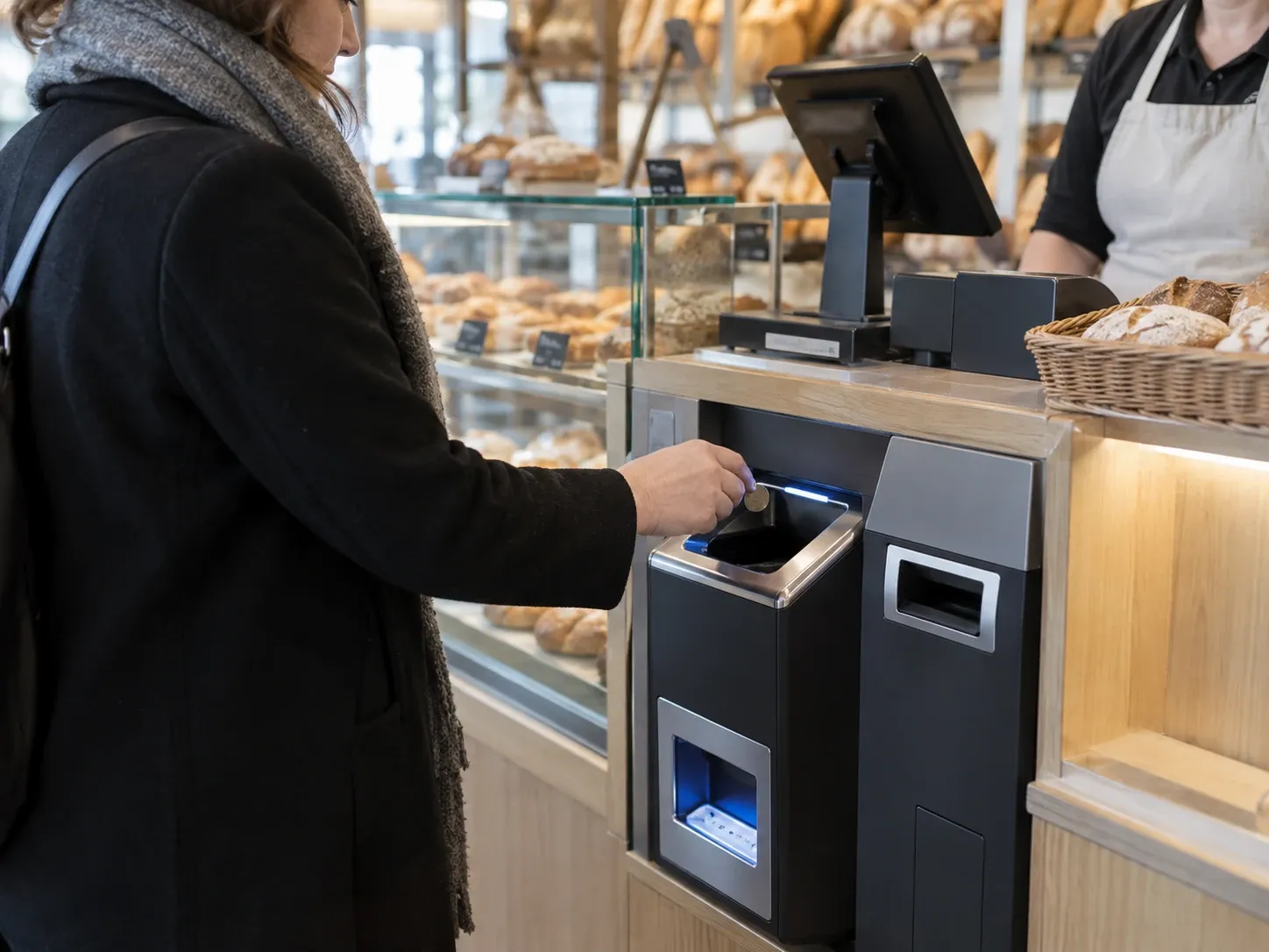 Une cliente insère une pièce dans un monnayeur automatique encastré au comptoir d'une boulangerie.