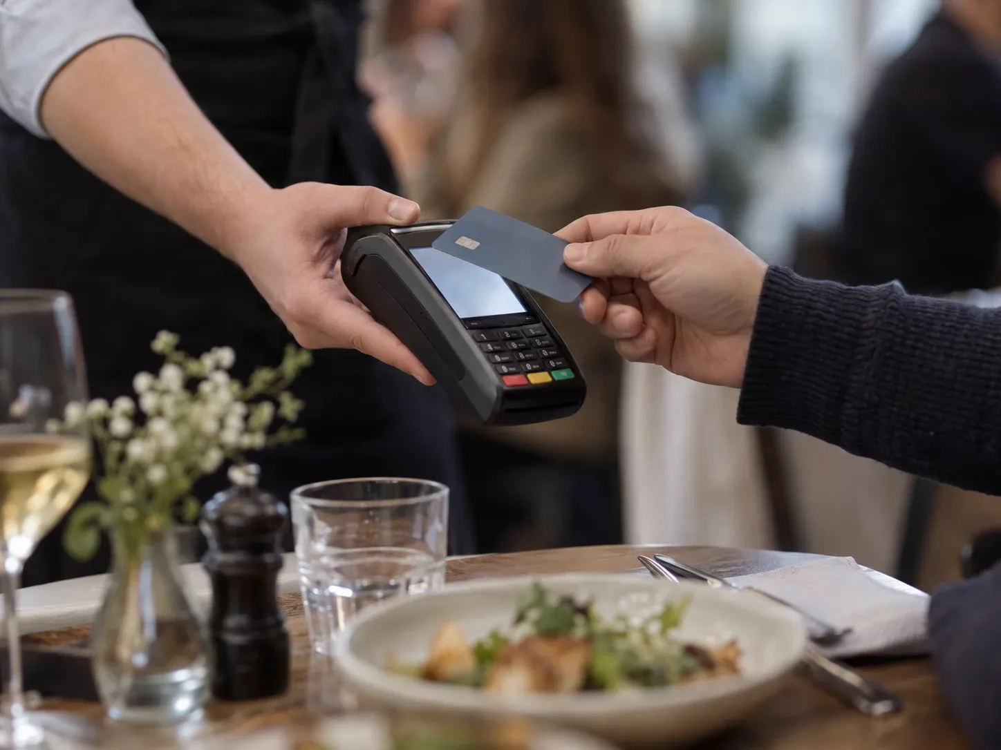 Un serveur présente un terminal de paiement portable à un client attablé, qui approche sa carte.